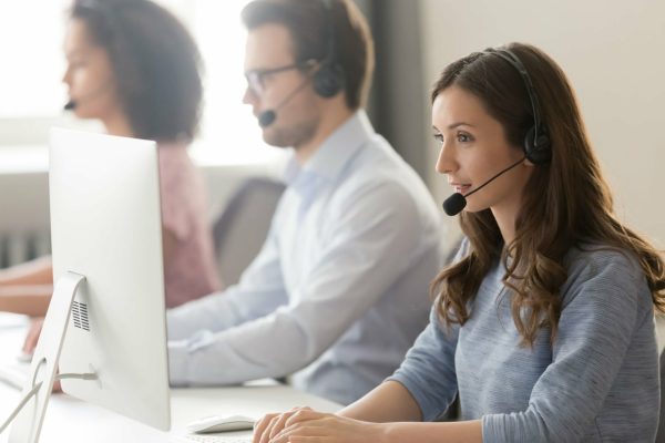 Millennial female call center agent wear headset with microphone consult customer online on pc in coworking space, focused woman employee in earphones busy working on computer in shared office